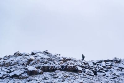 A trail runner crosses a rocky ridge covered in snow in the Lunch Loops trail system.